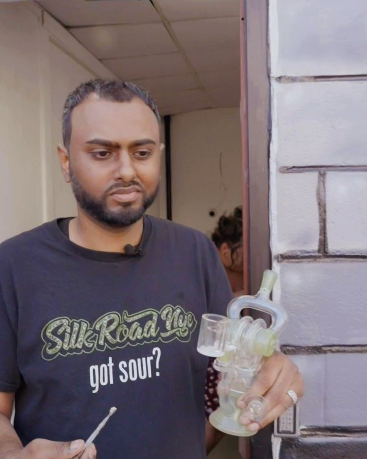Live dab demonstration at Silk Road NYC's 710 event — presenter with lapel mic holding a glass rig and dab tool, wearing the Silk Road NYC 'got sour?' tee